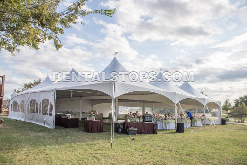 A large outdoor tent set up for an event, featuring multiple tables decorated with flowers and tablecloths, on a grassy area under a partly cloudy sky.