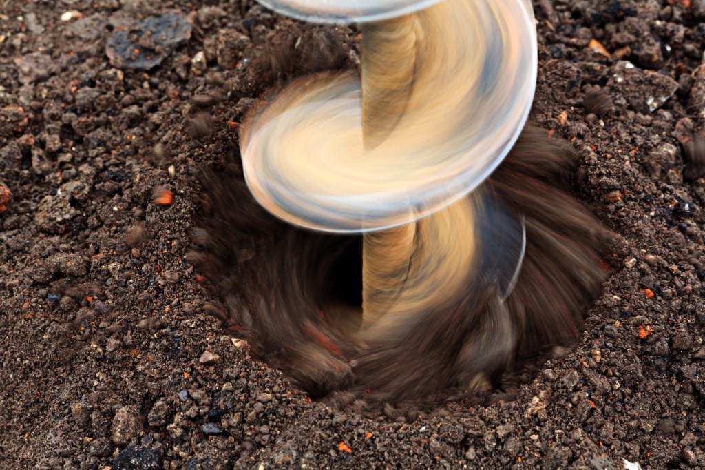 A close-up view of an auger drilling into the soil, showing swirling dirt being extracted from the ground.